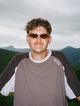 Harrie stands in front of a valley with pink sunglasses on staring at camera