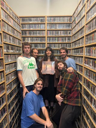 Situated in the music library where each wall is made up of shelves holding CDs, all five members of Intermood stand around Solstice host Hannah Galvin as she holds their debut EP on vinyl in front of her chest.