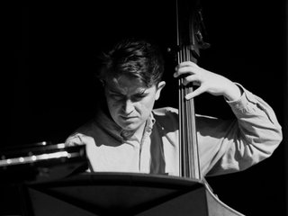 Black and white photo of musician Jacques Emery playing his double bass reading sheet music.