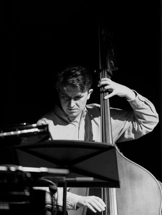 Black and white photo of musician Jacques Emery playing his double bass reading sheet music.