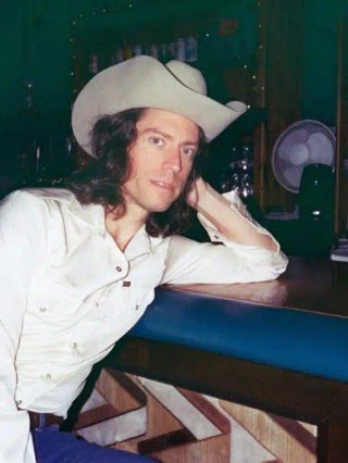 Man in white shirt and cowboy hat leaning on a bar