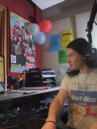 Jim Kretschmer is attentive to their computer in the studio. They are typing and looking at the screen and wearing a shirt that says "Yeet-Bicc"