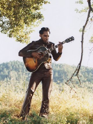 Leon Bridges. Man in sunlit field playing guitar