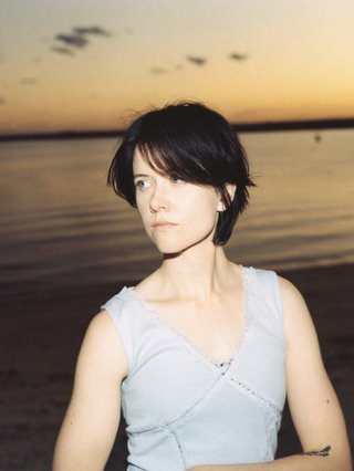 georgia mulligan stands in front of an ocean at sunset, she is wearing a grey tank top