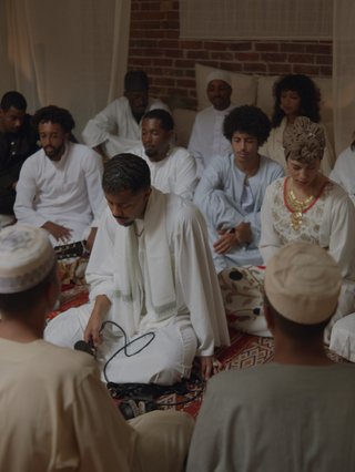 Mustafa sits int he centre of a group. They are in all white in a prayer and song circle