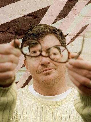 Man in white jumper holding glasses