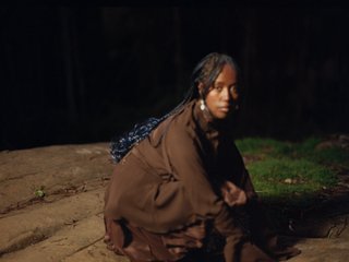 A slightly blurry image of Nū - crouching on a rock at night. She is looking at the camera
