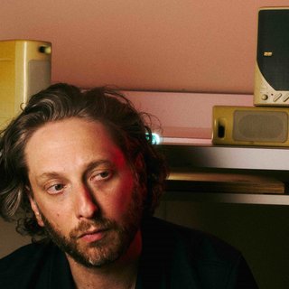 image of the artist Oneohtrix Point Never in a room. Behind his head is a desk with old speakers on top of it.