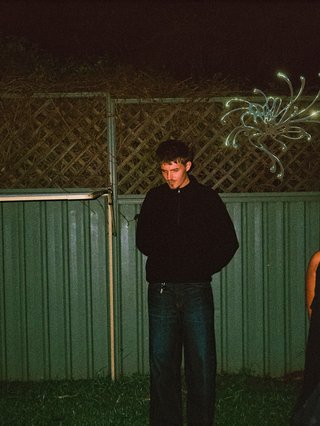 A greeny-grainy film photo of Bela, John and Bindi at night. They are standing in a backyard on grass, in front of a green fence