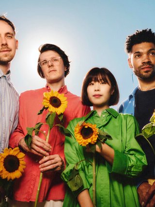 Four members of the band Phoebe Rings hold sunflowers against a blue sky.