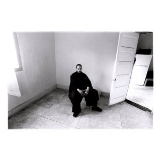 A black and white photo of Pink Siifu sitting in the corner of an empty room