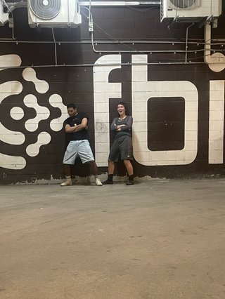 Alicia and Tim squat in the fbi garage. There's a grown painted wall with a huge fbi logo stencilled behind them