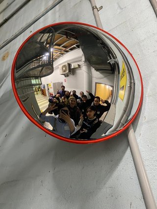 A photo of the Race Matters team taken in a rear view or "blindside" mirror. A bunch of people of colour huddled together looking at the mirror some of them are smiling and making peace signs with their hands.