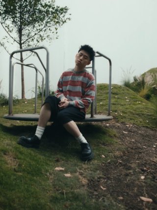 Rich Brian sits on playground equipment pensively, feeling ethereal in a misty setting