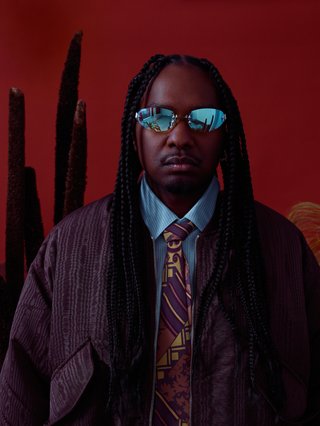 Man Standing in front of red back drop with sunglasses on