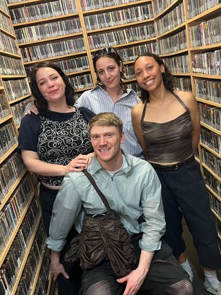 Three girls and a boy pose for a photo among shelves of music