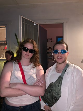Woman with black sunglasses and crossed arms is standing next to a man with swimming goggles
