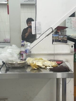 a mirror selfie in Ashfield buns shop, shareeka is blurry with some kitchen prep and pomelo peeled in the foreground