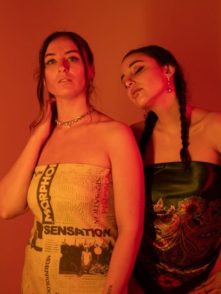 Naomi Robinson and Poli Pearl of Western Australian born band Special Feelings stand side by side under dim red lighting wearing strapless tops looking away from the camera.