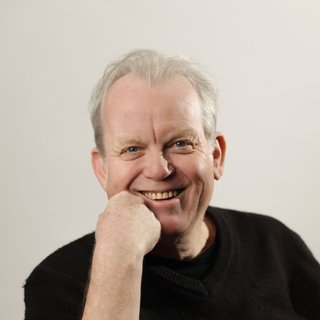 Stuart is smiling charmingly, wearing a black t-shirt against a stark white background.