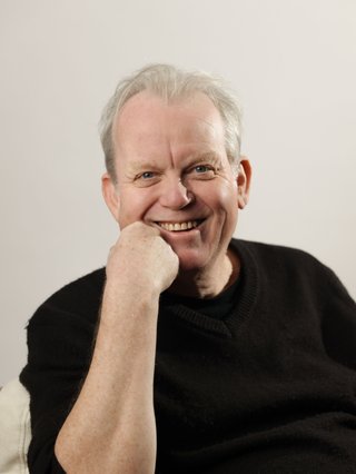 Stuart is smiling charmingly, wearing a black t-shirt against a stark white background.