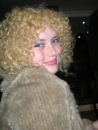 A digital camera photo of Zara looking to her right at the camera, smiling. She is wearing a light brown jumper and holding a wine glass.