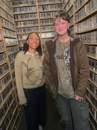 two people stand in front of cds on shelf