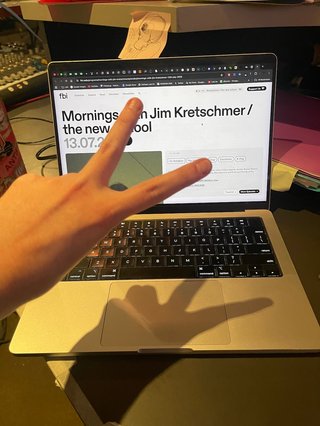 A picture of a laptop displaying the fbi.radio website. There is a hand in front of the screen making a peace sign.