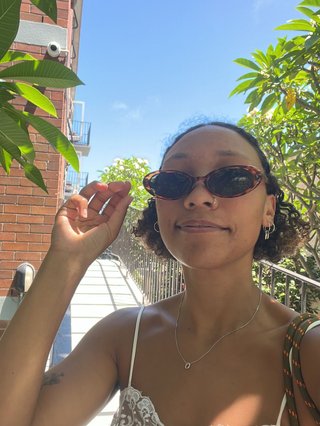 bri smiling and wearing glasses, standing in front of a frangipani tree