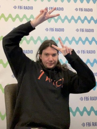 Jim throwing up a pair of peace signs in front of an fbi branded wall in the studio.