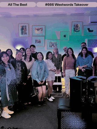 A group of women and some guys gather together in a room with some black speakers (bottom right) and some nice paintings on the wall behind them