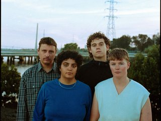 A film photo of the four members of the band dogworld standing outside together, all looking at the camera with neutral expressions.
