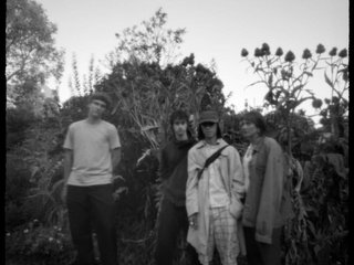 A blurry black and white photo of the band standing in an overgrown garden