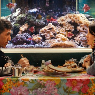 Scene from 'No Good Men' film with two actors sat at a table eating. There is an aquarium behind them.