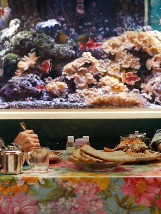 Scene from 'No Good Men' film with two actors sat at a table eating. There is an aquarium behind them.