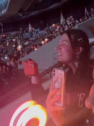 A side on picture of Jim in the audience at Marvel Stadium. They are smiling brightly at seeing one of their favourite songs being performed.