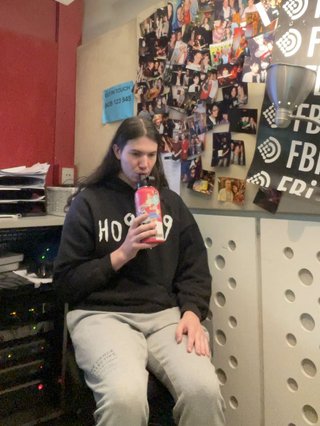 Jim sitting in the fbi studio, drinking out of their water bottle with a blank look on their face.