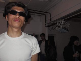 piiico puts at the camera flashing on him in a dark room. He is wearing sunglasses and a white tshirt.