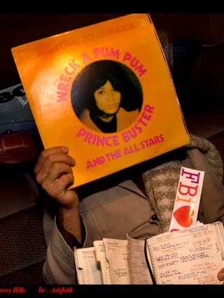 Jack is photographed in a car holding up a record to his face using his right hand. He is holding a notebook and 'FBI Radio' sticker in his left hand