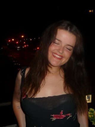 Freya's eyes are closed as she smiles and poses for the camera. She is wearing a black floral dress