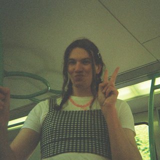 Jim Kretschmer in a really cute outfit with cute braids, standing on a train holding up a peace sign.