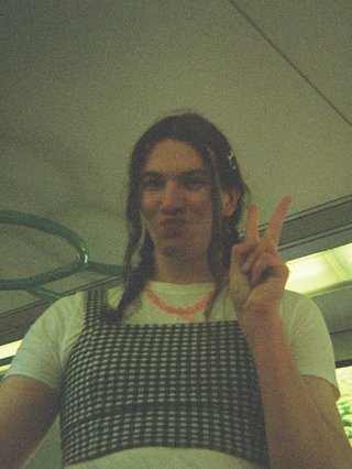 Jim Kretschmer in a really cute outfit with cute braids, standing on a train holding up a peace sign.