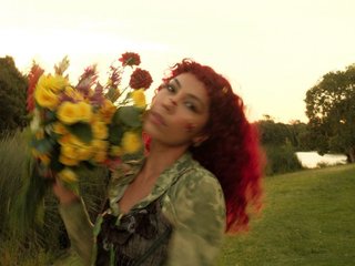 A woman with curly red hair in a field with a bouquet of yellow flowers.