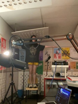 Jimothy standing on a chair on the far side of the studio, T-posing in a slightly unsettling fashion.