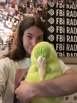 A selfie of Jim holding a plushie which is a lime green capybara holding a banana.