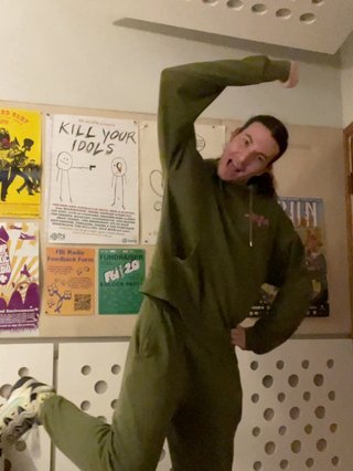 Jim with a hand on their hip, the other making a fist above their head and one leg up behind them mimicking the dance to "Gnarly", the hit new song from KATSEYE.