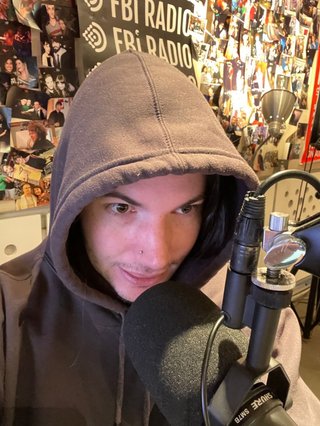 Jim, wearing a hood, posing at the studio microphone
