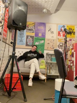 Jim sitting on the small couch in the studio. They have their legs crossed and are smiling at the camera.