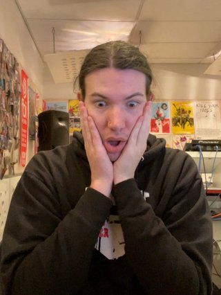 A picture of Jim in the fbi.radio studio, with their hands against their cheeks and a surprised expression on their face.