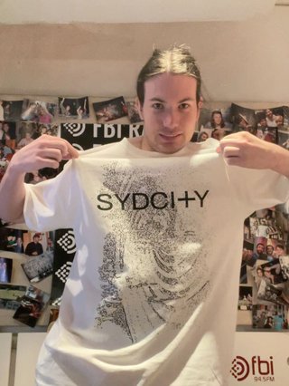 Jim in the fbi studio, showing off their white SYDCITY t-shirt.